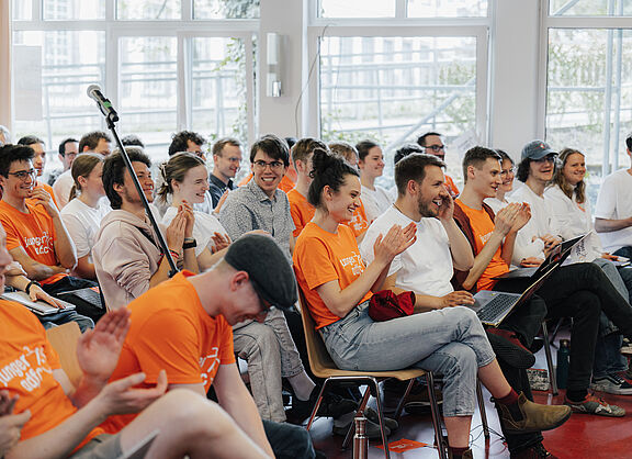 Junge Erwachsene sitzen in Stuhlreihen in einem Saal und heben grüne Stimmkarten in die Höhe.